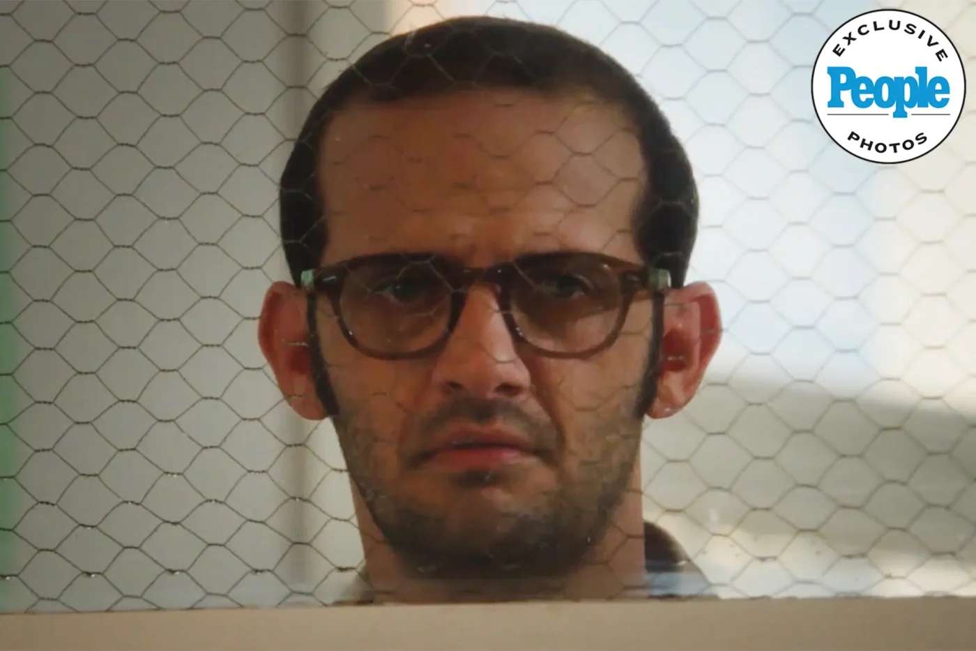 A person wearing glasses looking through a wire mesh screen featured in a People exclusive photo