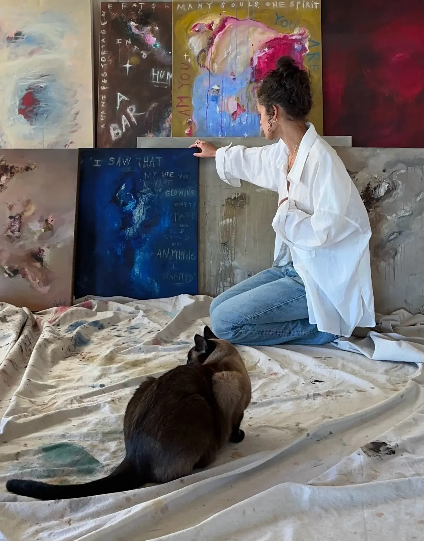 Aubrey Cleland painting with her Siamese cat, Simba, sitting in front of her.
