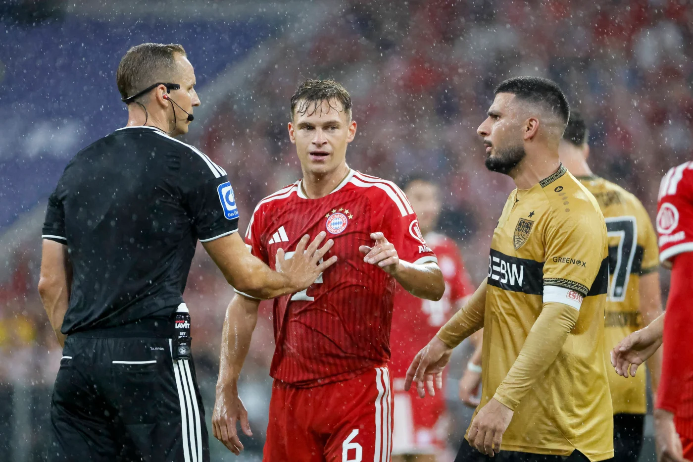 Bayerns Joshua Kimmich (M.) und Stuttgarts Deniz Undav (r.) diskutieren mit Schiedsrichter Sören Storks