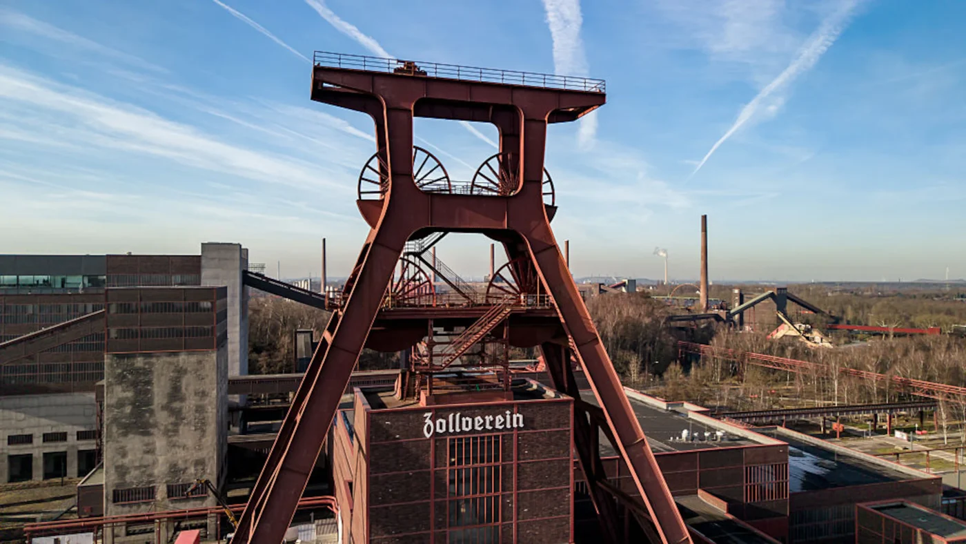 Drohnenaufnahme des ehemaligen Förderturms der Zeche Zollverein. Im Hintergrund blauer Himmel.