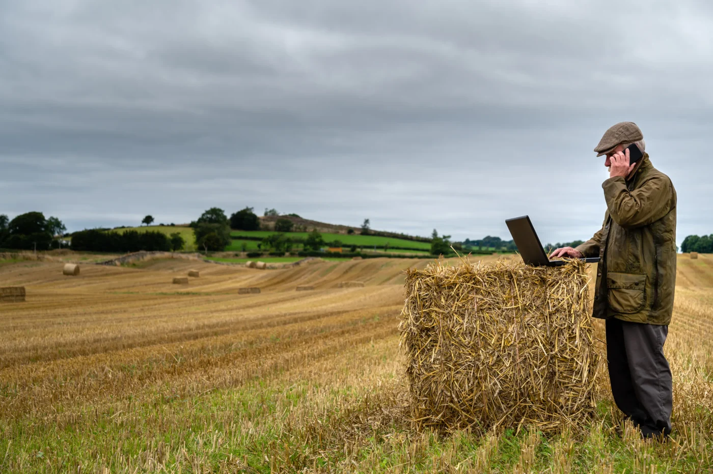 Ein Landwirt mit Handy und Notebook auf einem Acker.