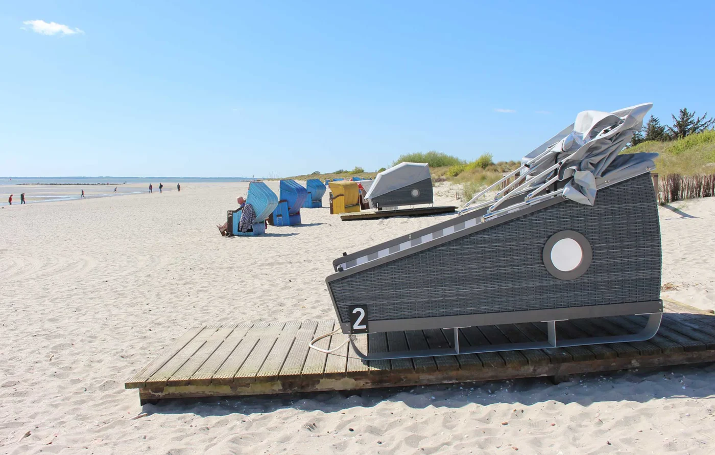 Ein Schlafstrandkorb steht am Stran, das Dach ist offen. Im Hintergrund stehen in einiger Entfernung weitere Strandkörbe und ein geschlossener Schlafstrandkorb.