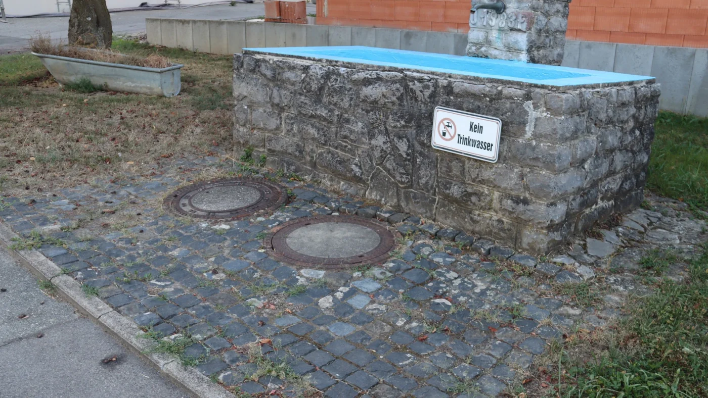 Eine bepflanzte Badewanne und ein abgeschalteter Trinkwasserbrunnen in Rohrdorf zeugen von Trockenheit.