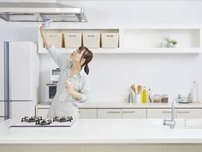 Eine Frau putzt eine Abzugshaube in der Küche.