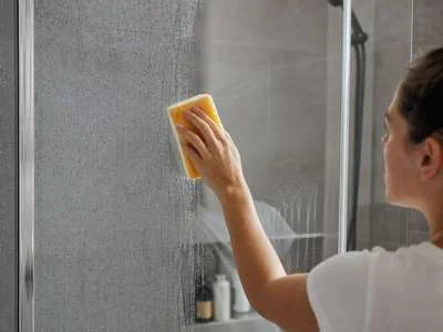 Eine Person putzt milchig gewordenes Glas in einer Dusche.