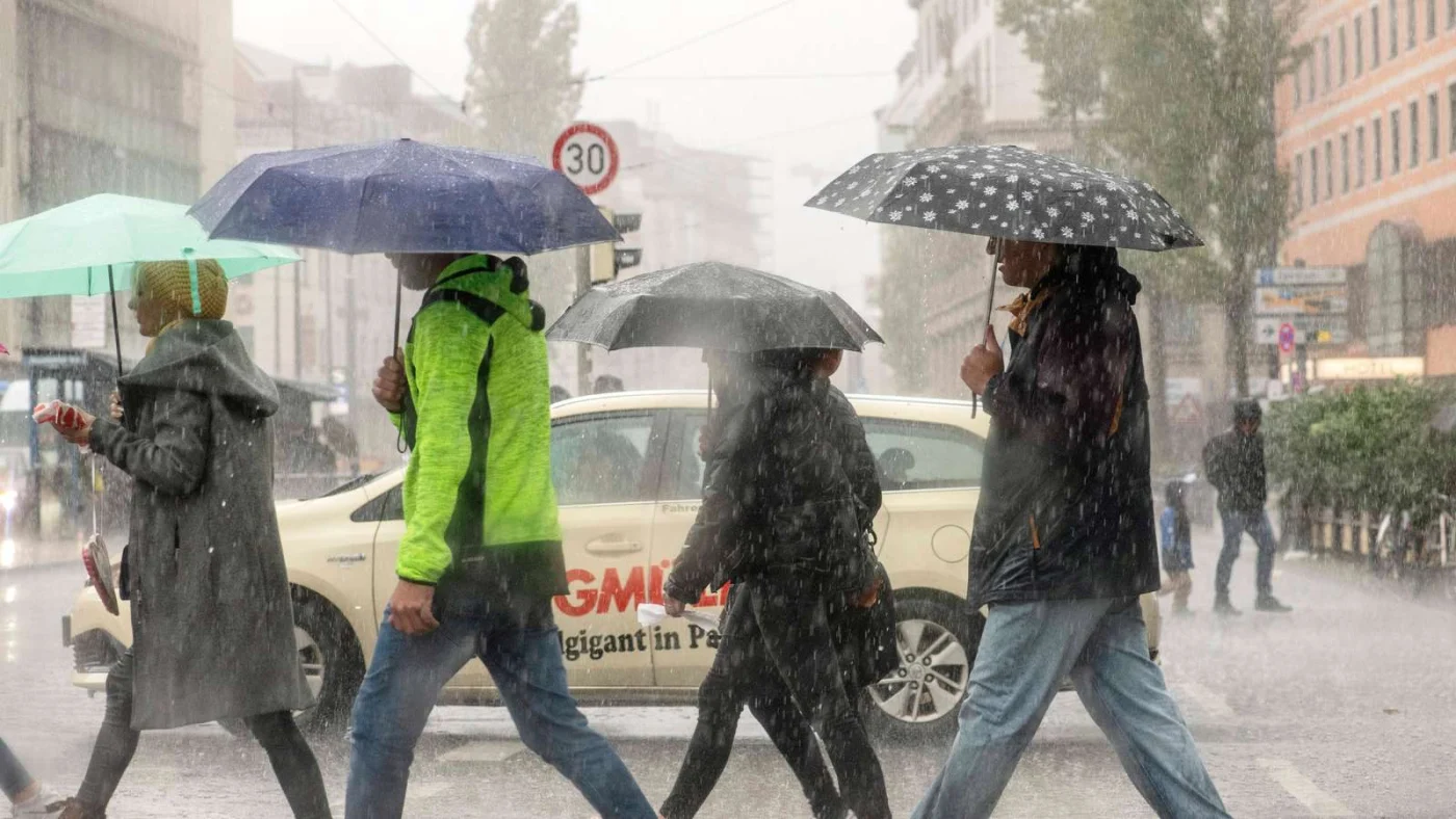 Fünf Passanten überqueren in strömendem Regen die Straße