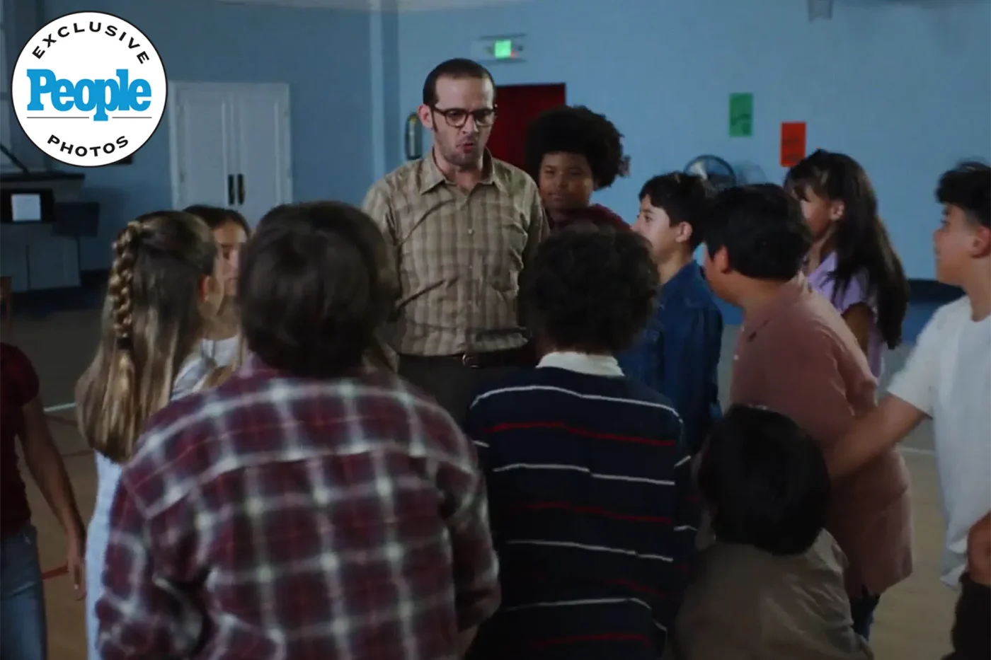 Group of children gathered around an adult man in a classroom or school setting