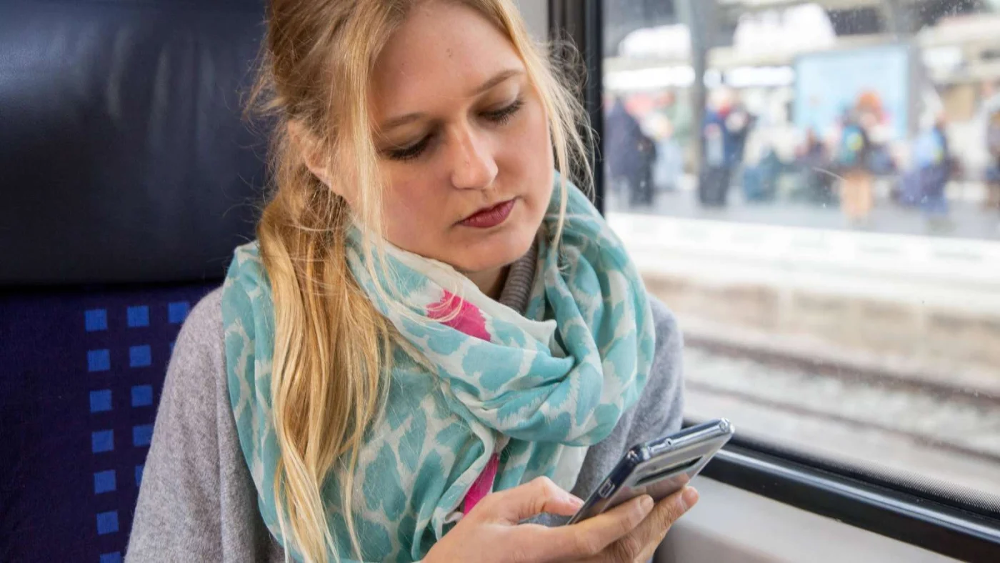 Junge Frau im Zug blickt auf ihr Smartphone.