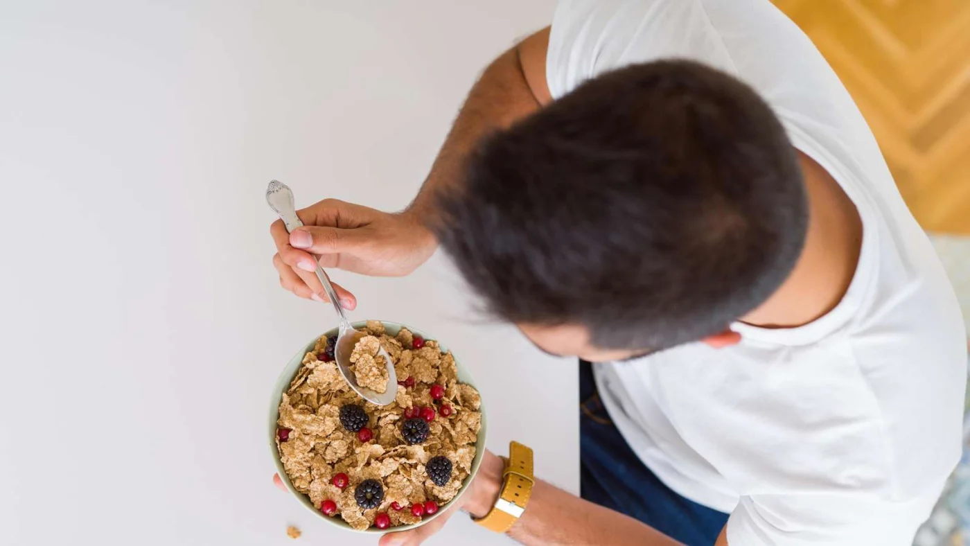 Mann isst aus Schüssel mit Frühstückszerealien.