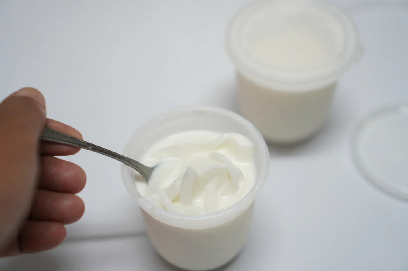 Nahaufnahme einer Person, die aus einem Plastikbecher Joghurt ist.