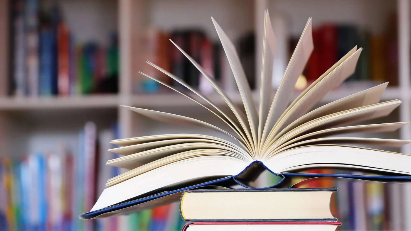 Nahaufnahme von einem aufgeschlagenen Buch, dahinter unscharf ein Bücherregal - Sachbücher für Ostern (Symbolbild)