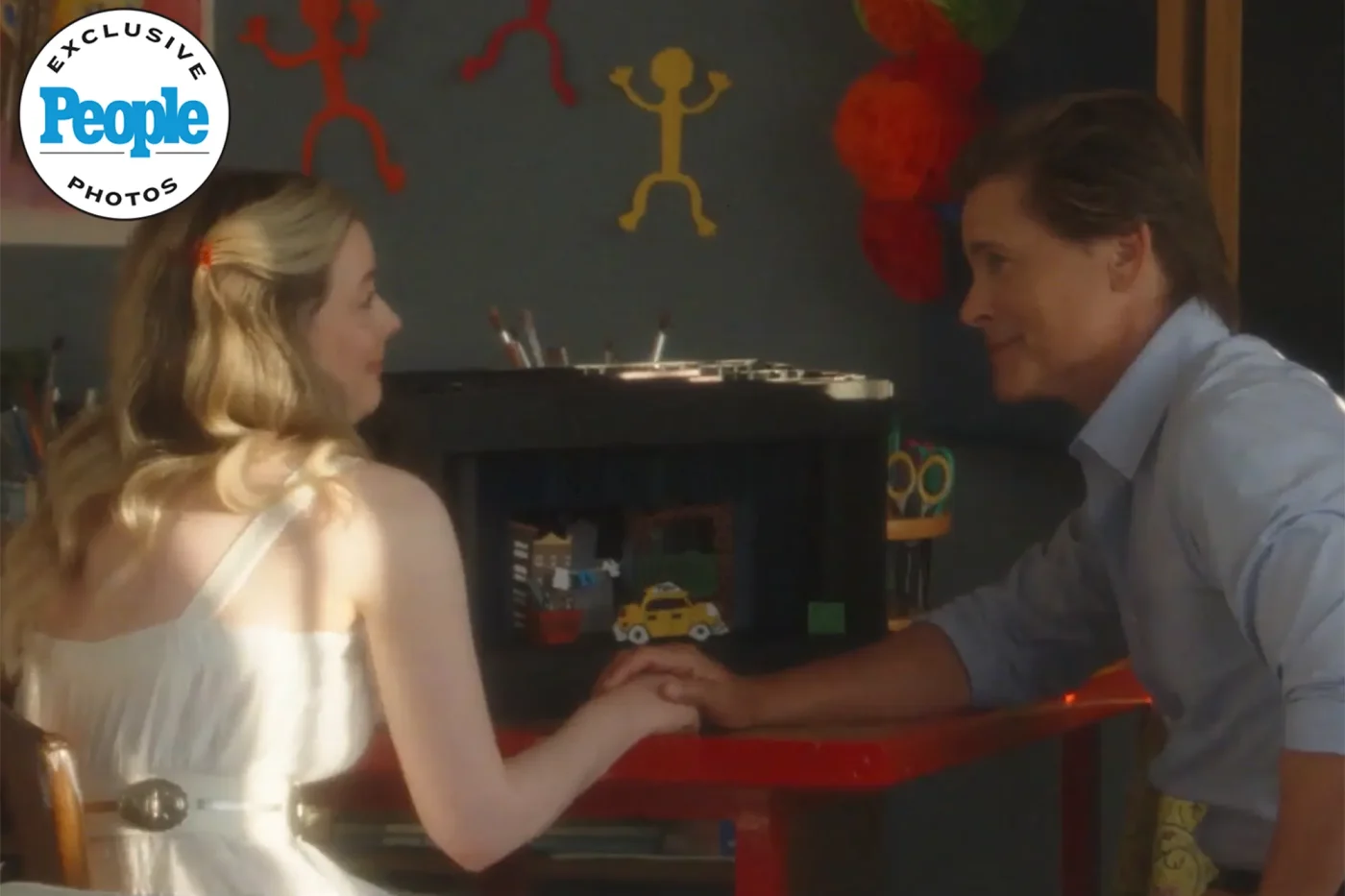 Rob Lowe seated at a table facing a woman while holding hands