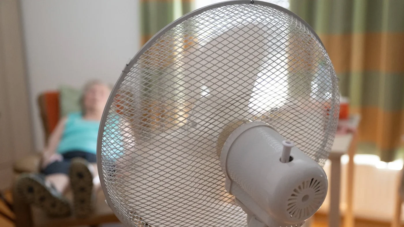 Seniorin liegt auf Sessel und kühlt sich mit Ventilator ab