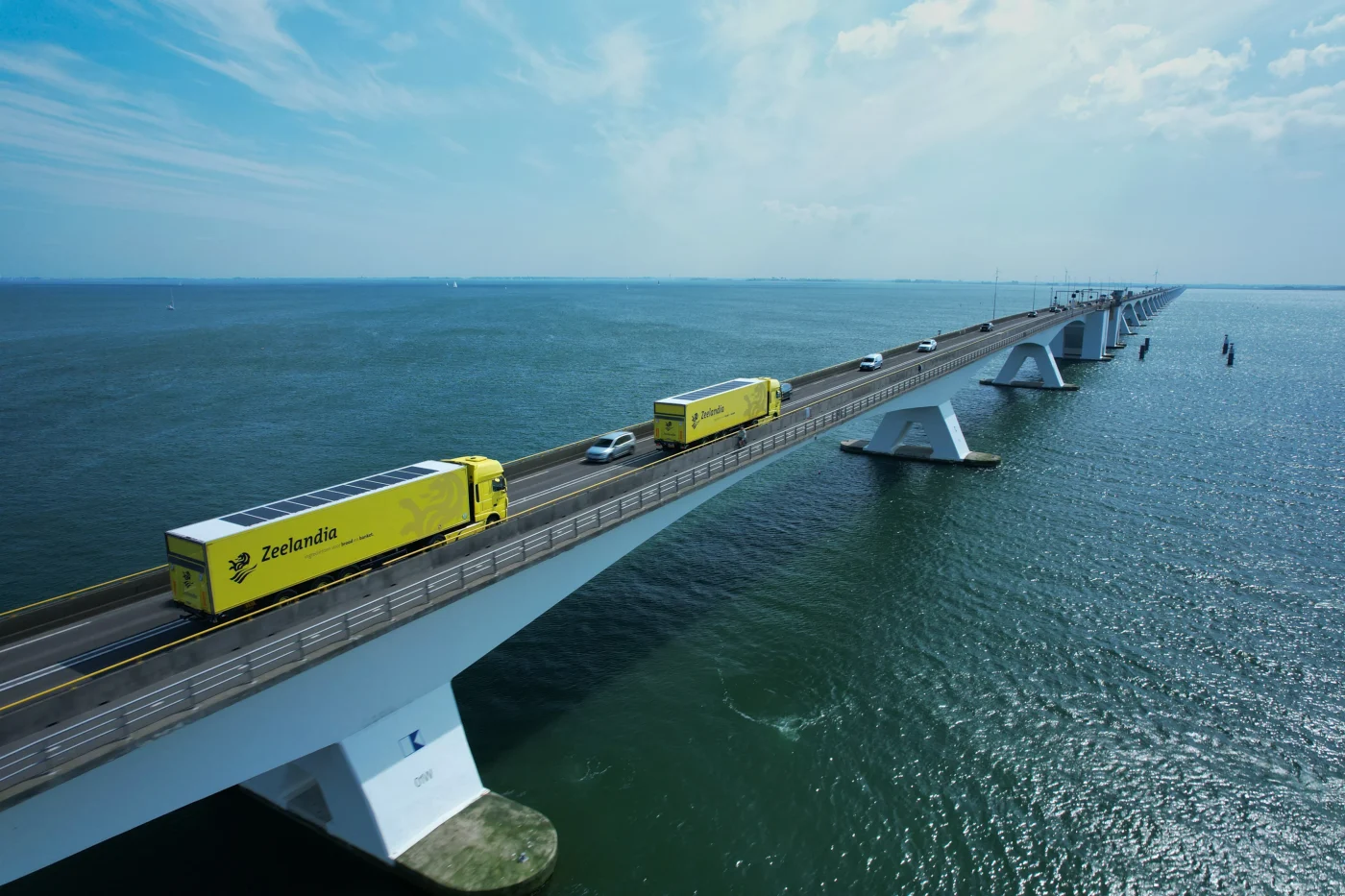 Zwei Lkw mit Solarmodulen auf den Aufliegern fahren über eine Brücke.