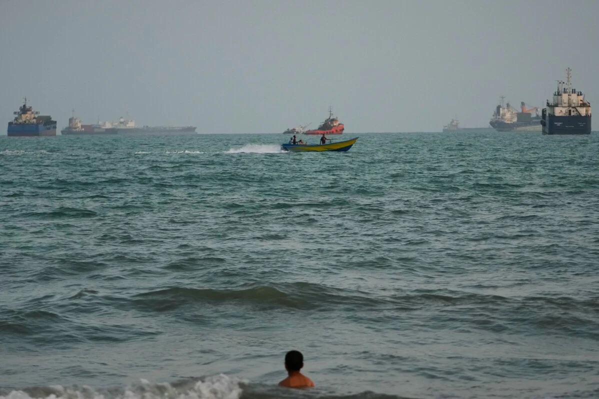 A swimmer remains near the shore as a motorboat passes commercial vessels anchored in the Strait of Hormuz off Bandar Abbas, Iran, Friday, Sept. 4, 2026. (AP Photo/Vahid Salemi)