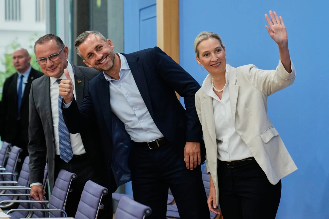 AfD-Co-Chefin Alice Weidel winkt, Tino Chrupalla zeigt Daumen hoch, Ulrich Siegmund lächelt bei Pressekonferenz in Berlin.