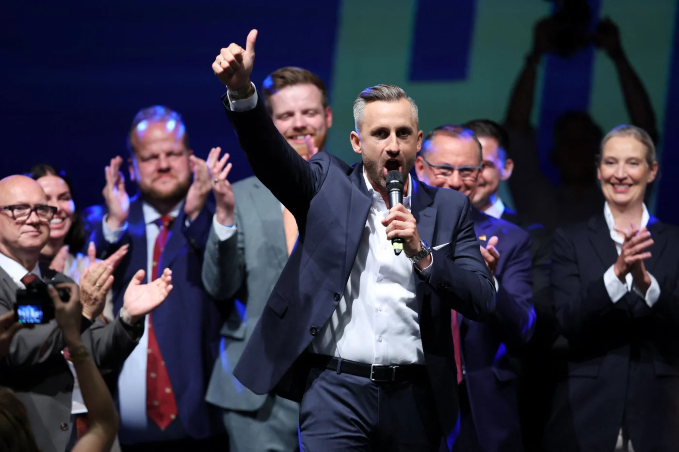 AfD-Spitzenkandidat Ulrich Siegmund hält Mikrofon, reckt Daumen hoch, umgeben von applaudierenden Parteianhängern bei der Wahlparty in Magdeburg.