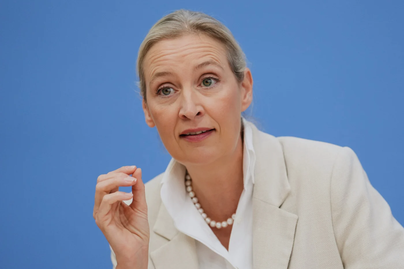 AfD-Vorsitzende Alice Weidel spricht an einer Pressekonferenz in Berlin, gekleidet in cremefarbenem Blazer und Perlenkette.