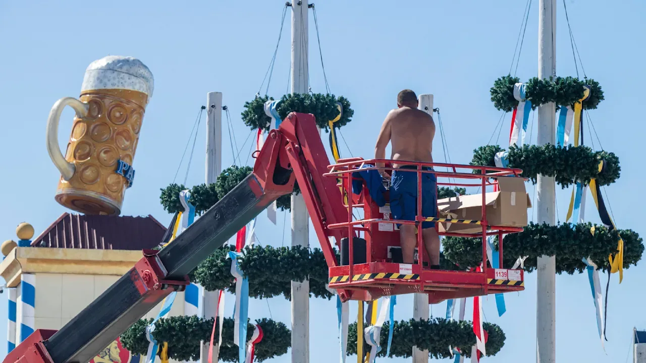Ein Arbeiter bedient am Freitag auf der Theresienwiese einen Hubsteiger, um letzte Arbeiten an den Maibaumspitzen zu erledigen