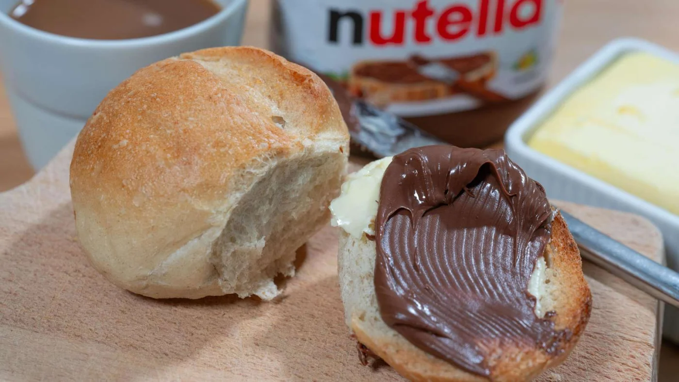 Ein Brötchen mit Nutella liegt auf einem Frühstücksbrett