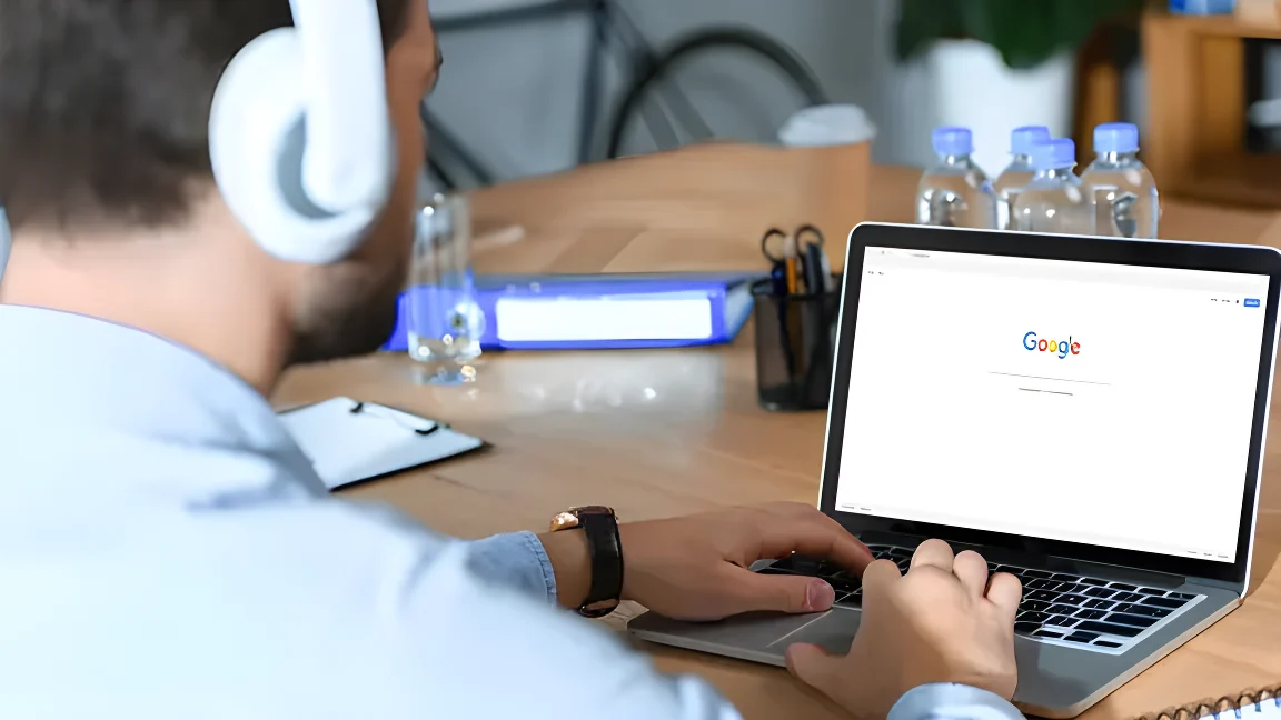 Ein Mann sitzt mit aufgesetzten Kopfhörern vor einem Laptop, der die Website von Google zeigt