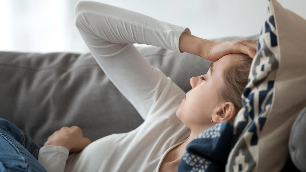 Eine Frau liegt mit Kopfschmerzen auf dem Sofa