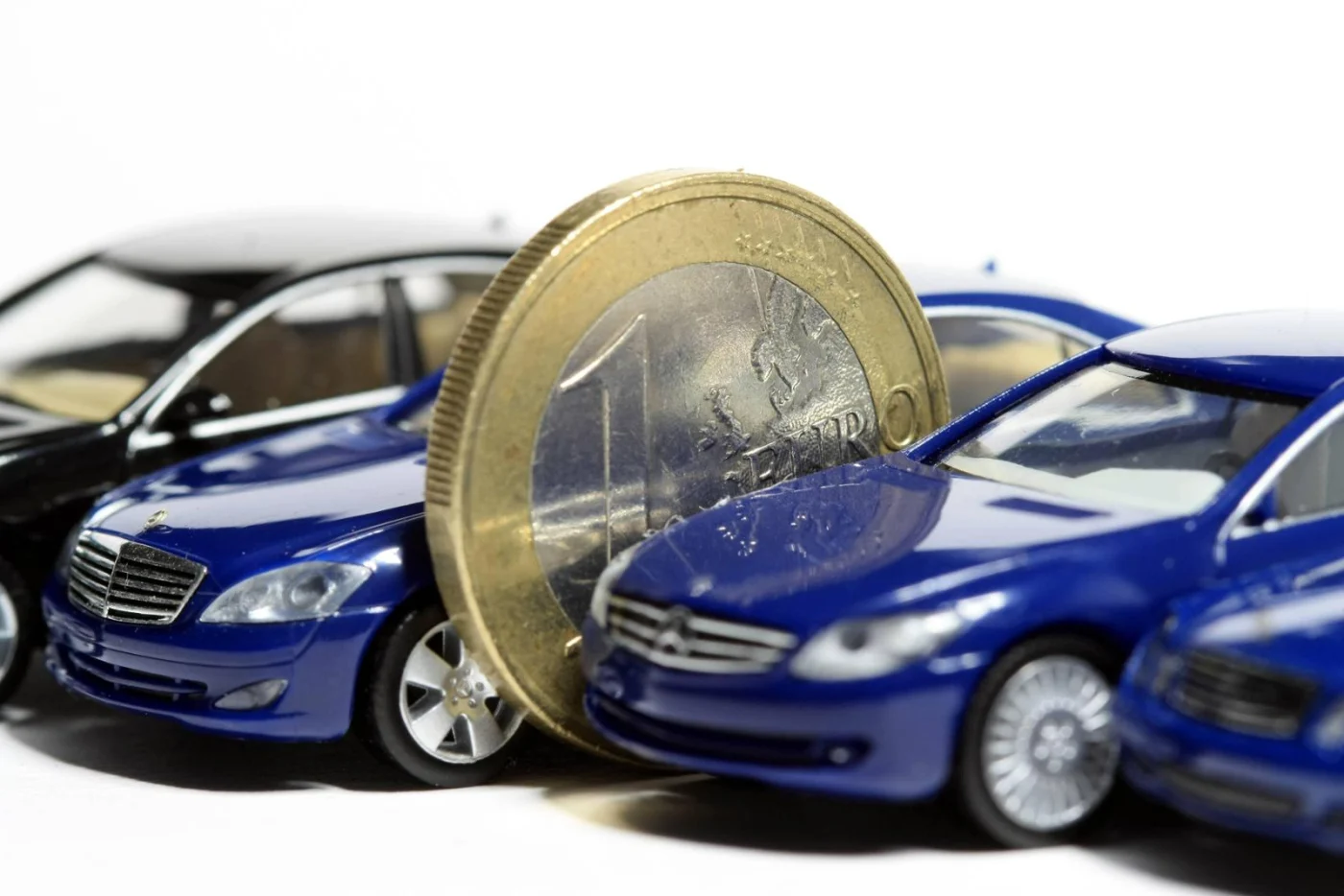 Euro Geldmünze steht zwischen einem Fuhrpark aus Miniaturautos (Symbolbild)