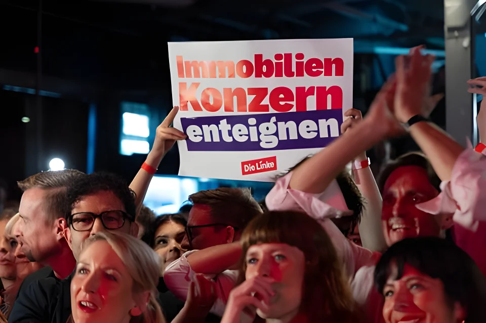 Man sieht mehrere Politiker:innen der Berliner Linken, eine Person hält „Immobilienkonzern enteignen“-Schild hoch
