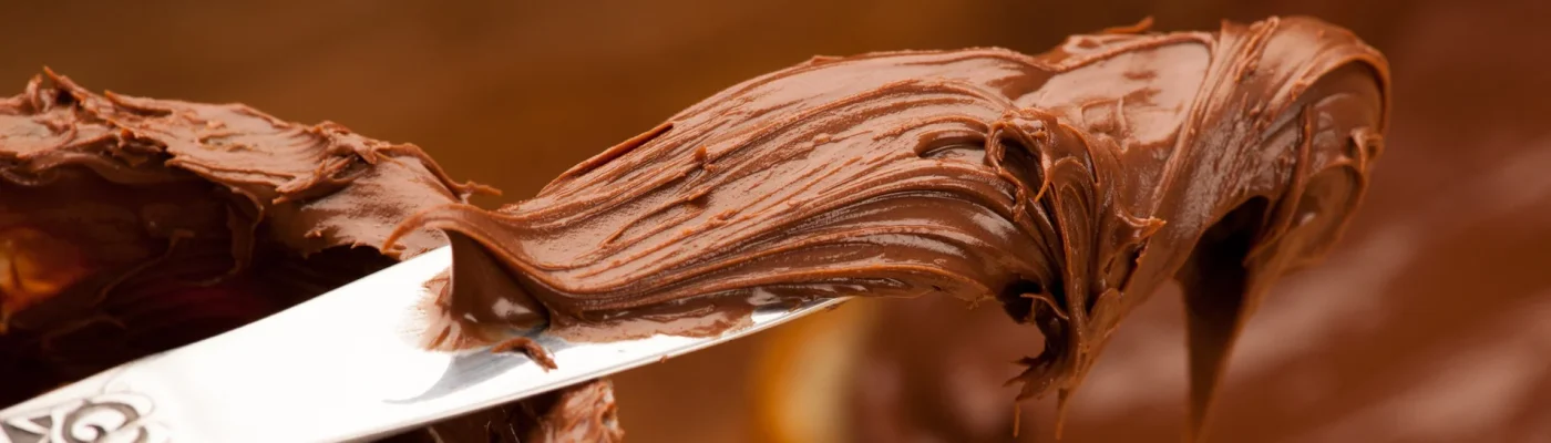 Nuss-Nougat-Creme auf einem Buttermesser. Stiftung Warentest hat herausgefunden, dass ein Discounterprodukt besser ist, als das Markenprodukt Nutella