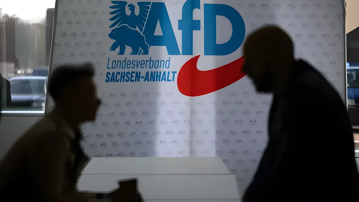 Teilnehmer des Landesparteitages der AfD Sachsen-Anhalt in Magdeburg unterhalten sich vor einer Wand mit dem Parteilogo.